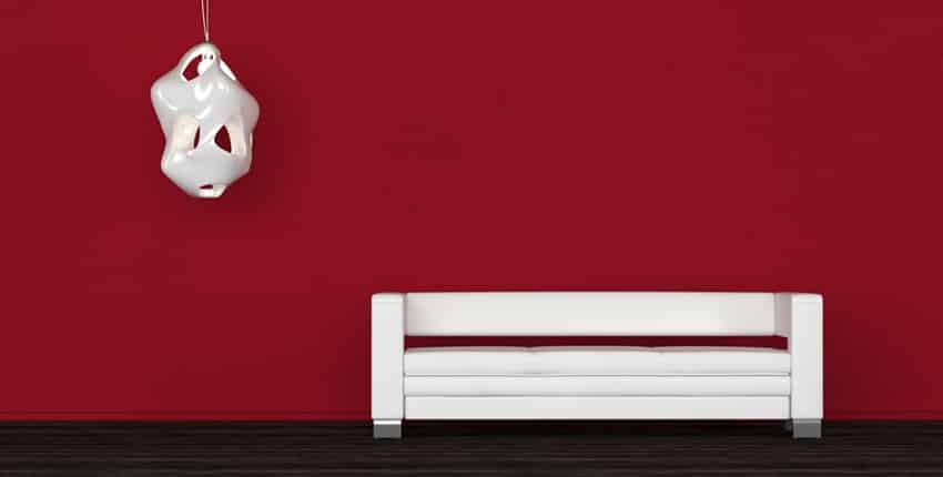 Comfortable white sofa in a red room standing against the wall below a wall sconce on a black floor in an architectural background ready for your interior decorating ideas. 3d Rendering.